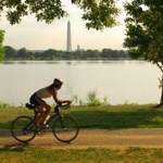 Cyclist rides along a path with the National Monument in the background.