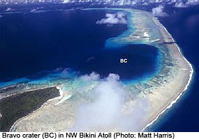 An aerial photo of a tropical atoll in which there is a crater labeled BC created by a nuclear bomb blast.
