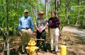 3 men standing in front of a yellow fire hydrant in the forest