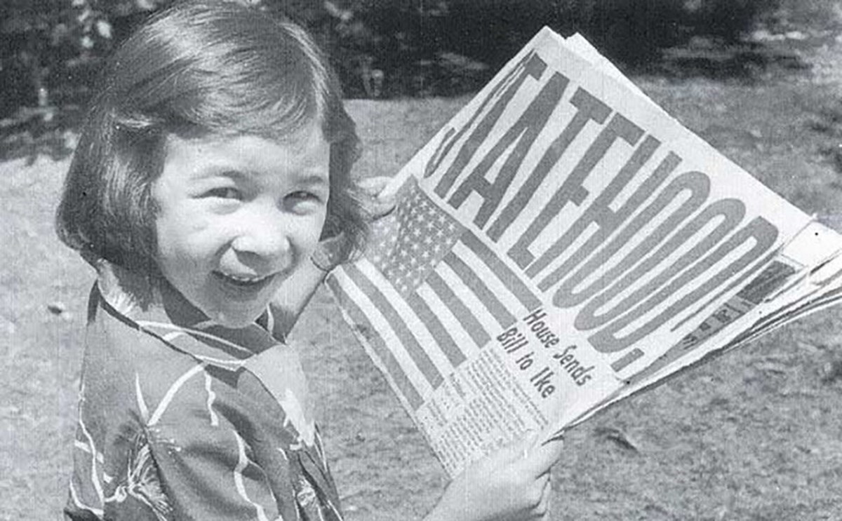 black and white historic image of a little girl holding a newspaper with a large headline reading "Statehood"