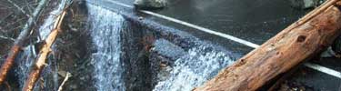 Water falls over sheared roadway covered with landslide debris