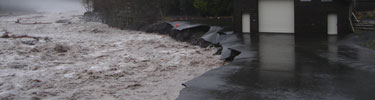 The rain swollen Nisqually River undercuts pavement and a building foundation at Longmire.