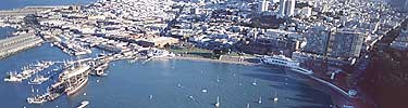 An ariel view south across the Aquatic Park lagoon with the pier on the left, museum on the right, and SF skyline in the background.