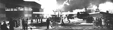 Clean up begins on Ford Island. Smoke from the USS Shaw in the background.