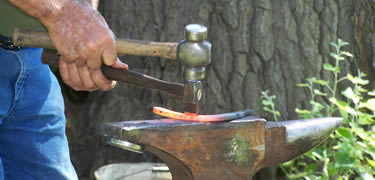 Hammer comes down on hot metal being worked by blacksmith