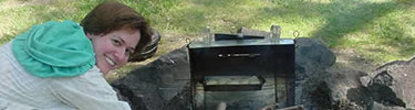 Woman in pioneer dress cooking over open fire.