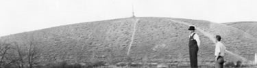 historic photo: officials looking over grounds in 1936, hill with monument on top in the background.