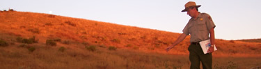 Ranger leading walk at sunset, landscape is bathed in evening light, moon is rising over hill.