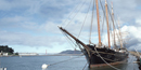 A view of the long, pointed bowsprint of the schooner THAYER that extends from the bow over the water.