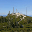 Telecommunication towers and buildings on summit of Shasta Bally surrounded by shrubs and sandy areas with trees in foreground