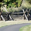 paved path passes by tall grass and split rail fence