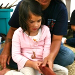 Teaching child to pound kapa (barkcloth)