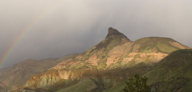 Image of Sheep Rock with a rainbow and clouds.