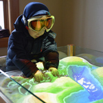 A young winter visitors digs his hands into an augment reality sandbox