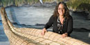 A woman seated behind a tule reed canoe. A woman seated behind a tule reed canoe.