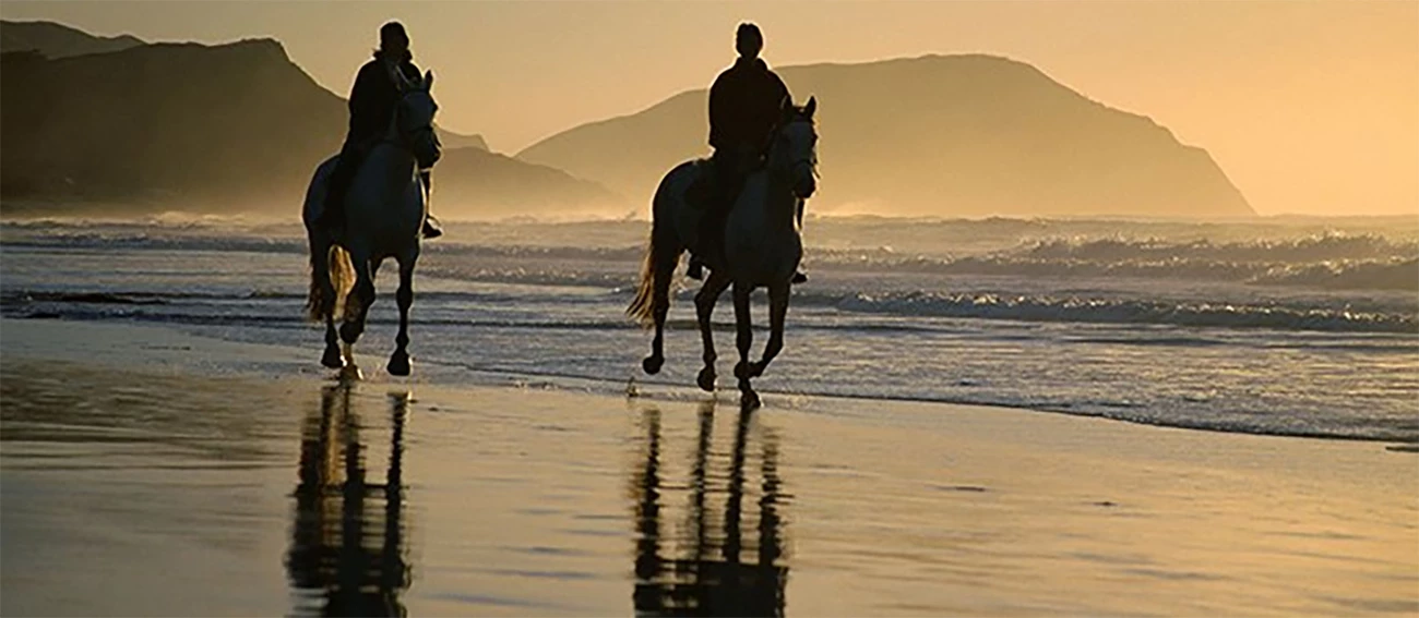 Horses on the Beach Two people riding horses on the beach at sunset.