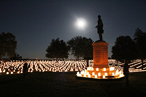 candles arrayed in rows across a moonlit landscape with a monument in the middle