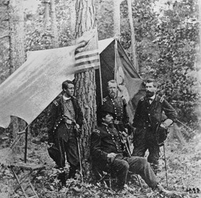 Four officers of the Union army, three standing, one seated, in front of a shelter.
