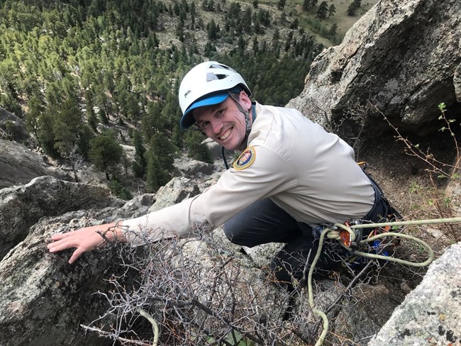 A climber looking up at the camera. He is wearing a long sleeve VIP shirt and white helmet.