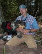 a researcher kneeling on the ground holds a young eagle in his hands
