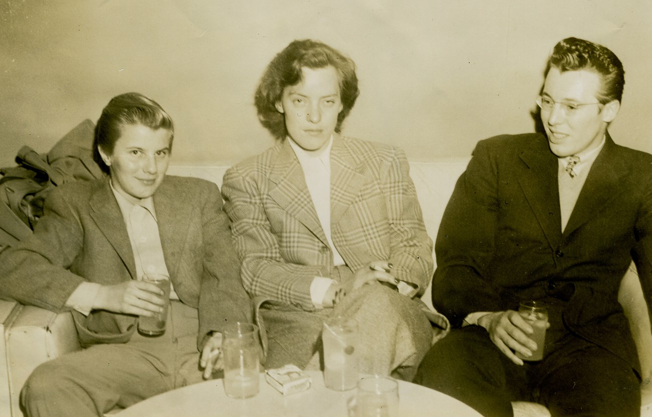 Three people are sitting on a couch in a lounge. Historic photo.