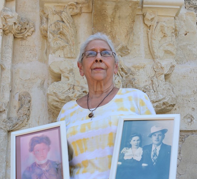 Woman posing and hold two pictures of her ancestors.