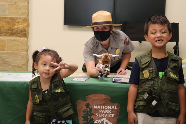 Two young junior rangers pose with a Park Ranger at the Visitor Center front desk.