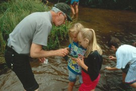 Uniformed ranger with two children looking at aquatic insects they have caught. Third child looking for insects.
