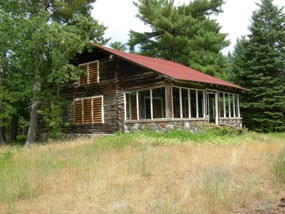 A log 1 1/2 story cabin with red roof and stone porch