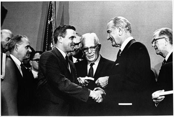 President Johnson hands Senator Mondale a box containing a pen as Chief Justice Earl Warren and others look on.