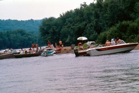 Four boats are pulled up on a sandy beach.  People are on the boats and standing on shore.