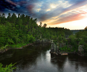 Green tree topped rocky gorge with river at sunrise 