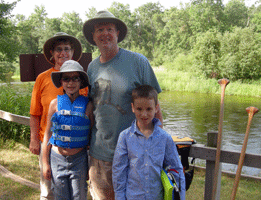 Two adults and two childreb stand along the river the children have lifejackets and canoe paddles can be seen