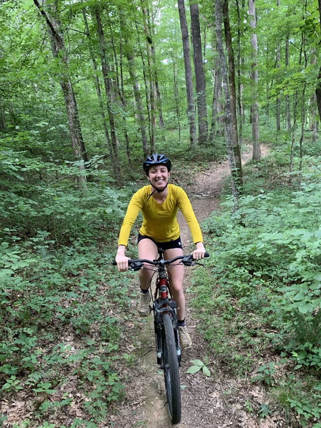 A young woman rides a bike through the forest.