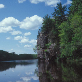 A grey Rock face emerging from the river against a blue cloudy sky. 
