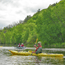 Yellow kayak with paddler, in background another kayak and high tree covered bluffs