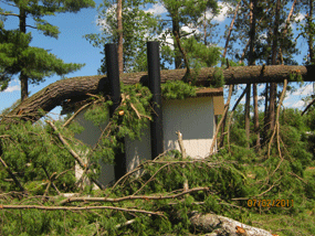 Broken trees and limbs are scattered around and on the still standing vault toilet building