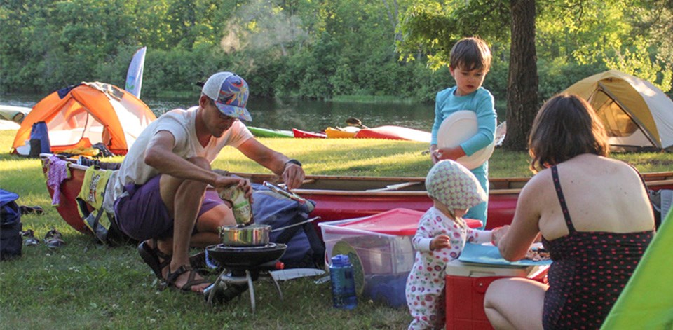 A family cooks near a tent next to a river.