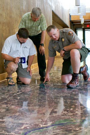A Park Ranger kneel over the river map on the floor talking with two visitors.