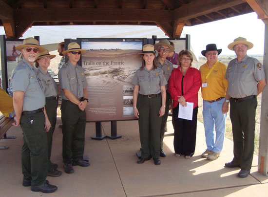 six park rangers and two others are standing on either side of an exhibit kiosk and facing you