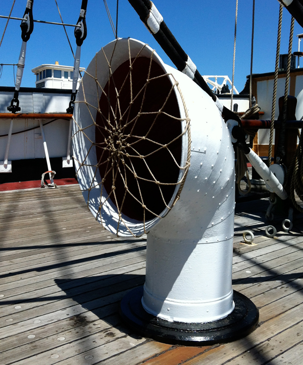 A white-colored ventilator with a large opening on the deck of a ship.