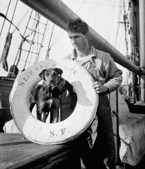 Man standing with his dog on the deck of a sailing ship. P50.76,542