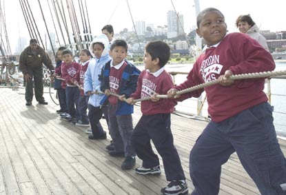 Children on the sailing ship Balclutha hauling on a line to raise a sail.