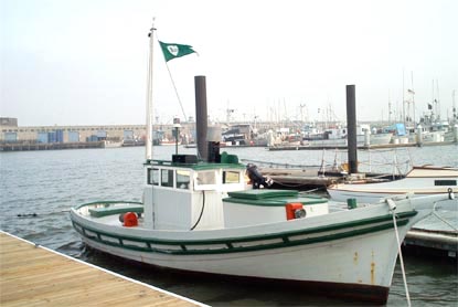 A Monterey fishing boat painted white and green floating in the water and moored at Hyde Street Pier.