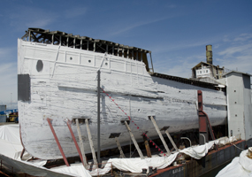 Wapama bow surrounded by sheeting, being painted white to encapsulate hazardous material.