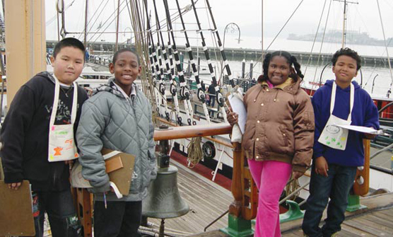 Four elementary school students standing on the deck of the sailing ship BALCLUTHA.