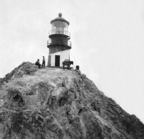 An historic photo of a lighthouse atop a rocky outcropping.