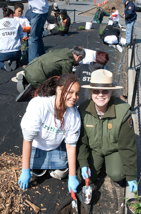 Children and park employees digging holes in the soil and planting native plants.