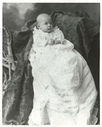 Black and white photo of the baby seated in a chair in a long white gown