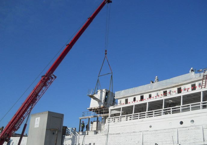 A mechanical crane lifting a pilothouse off a ship.